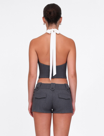 A woman with her hair in a bun is seen from behind wearing the TIGERMIST LOTUS TOP - CREAM : GREY, a dark gray cropped halter top with a white neck tie and matching high-waisted shorts, both in comfy stretch fabric. Background is plain white.