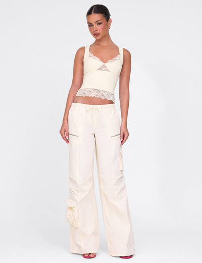 A person is wearing the Dione Lace Top in soft butter yellow by TIGERMIST, paired with high-waisted wide-leg pants featuring a drawstring. Their hair is styled up, echoing a sleek buttery finish, as they stand against a plain white background with relaxed arms.