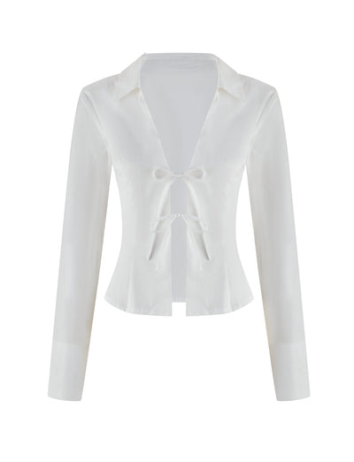 The BRIELLE SHIRT - WHITE by TIGERMIST is a white long-sleeve blouse with a deep V-neck and two front bow ties, offering a minimalistic, elegant design. Its soft stretch fabric is smooth, slightly glossy against the plain white background, and features a classic collar to accentuate its sophisticated charm.