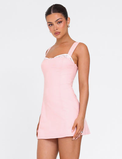 A woman models the TIGERMIST COLSON MINI DRESS in baby pink—sleeveless, fitted, with white lace trim at the neckline—against a plain white background.