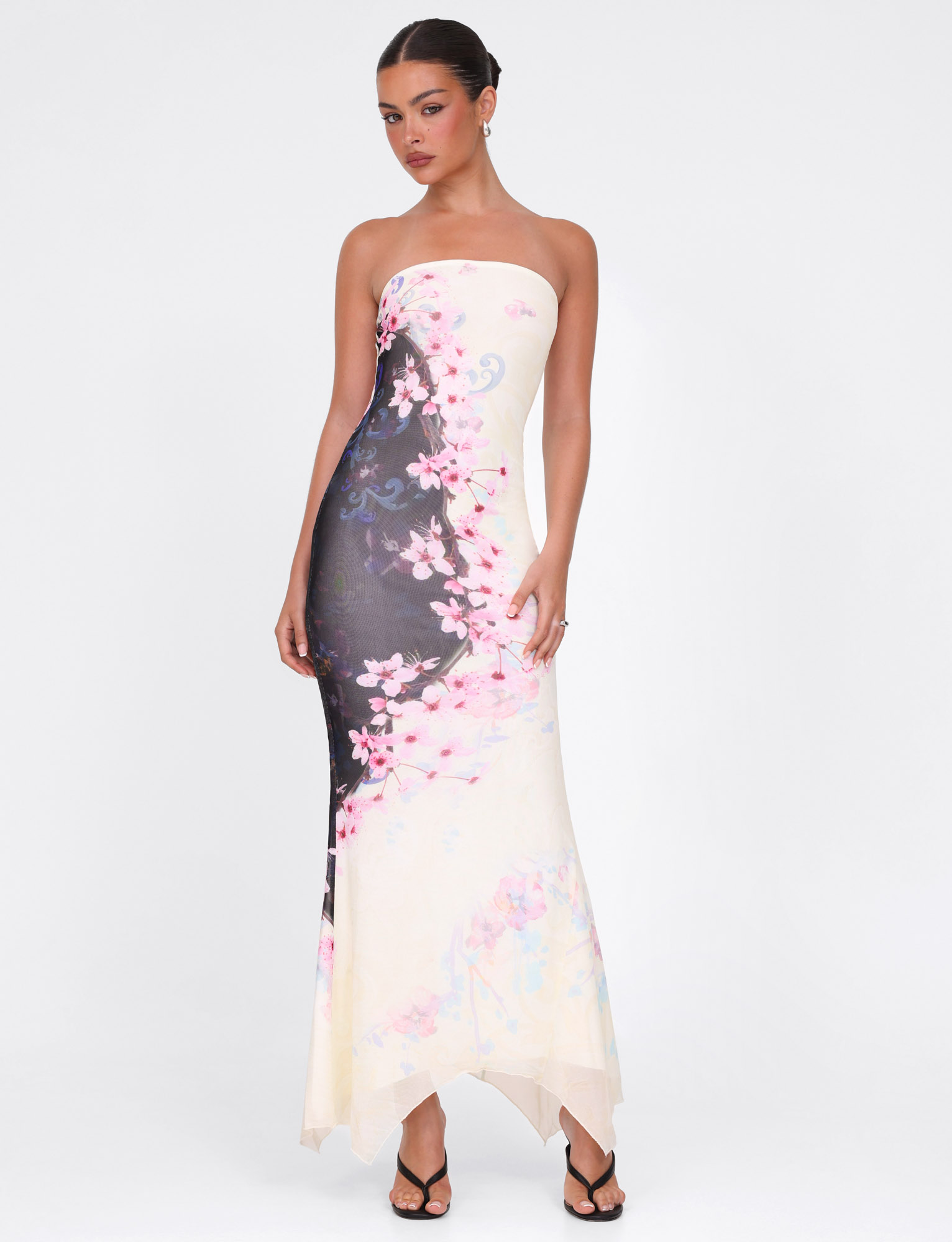 A woman stands against a white backdrop wearing the TIGERMIST LILLIAN MAXI DRESS in multi cherry blossom floral print, styled strapless with black strappy heels and her hands at her sides.