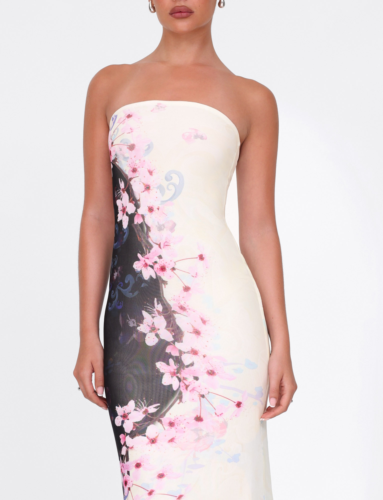 A woman models the TIGERMIST LILLIAN MAXI DRESS in Multi Floral Cherry Blossom, a strapless, high-stretch mesh dress with pink and white blossoms on cream. She stands against a plain white backdrop, her head partially out of frame.