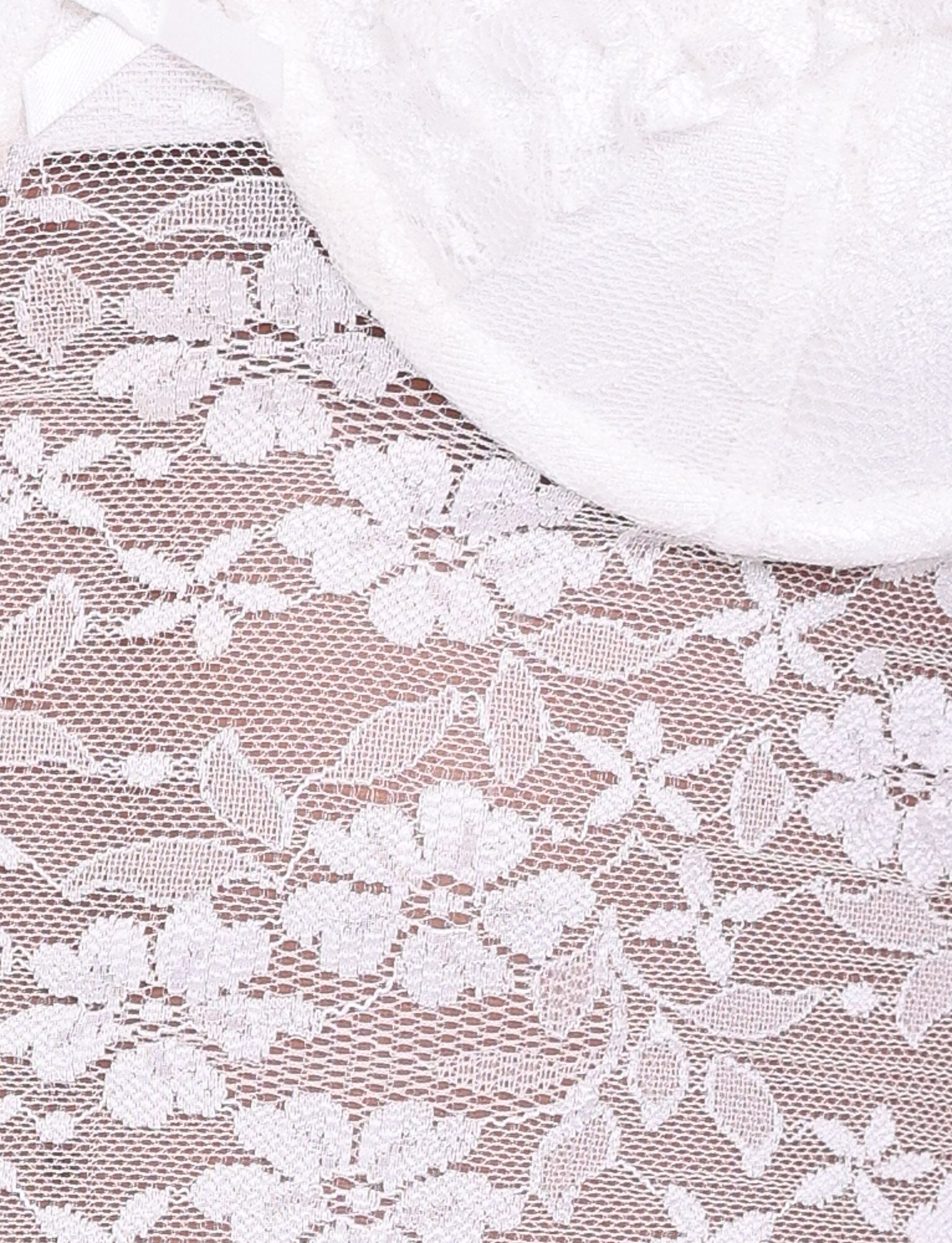 Close-up of the NYRA TOP - WHITE by TIGERMIST, featuring semi-sheer white lace with a floral pattern, partially covered at the top by a smooth, white curved fabric detail.
