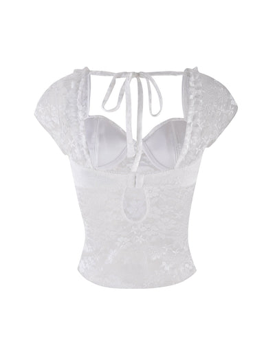 The NYRA TOP - WHITE by TIGERMIST is a white lace bustier with cap sleeves, open back, neck tie, and a keyhole at the lower back. Made from semi-sheer fabric with a delicate floral lace pattern.