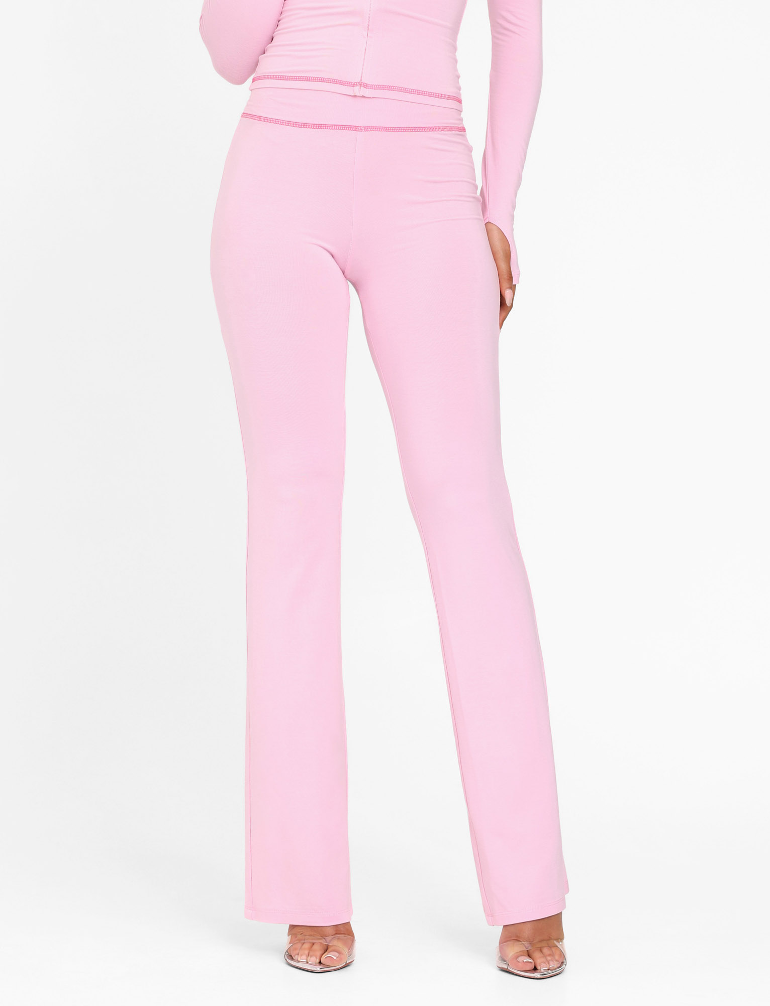 Wearing TIGERMIST’s BLAYZE PANT in soft pink, paired with a matching long-sleeve top and clear heels, this person poses against a plain white background.