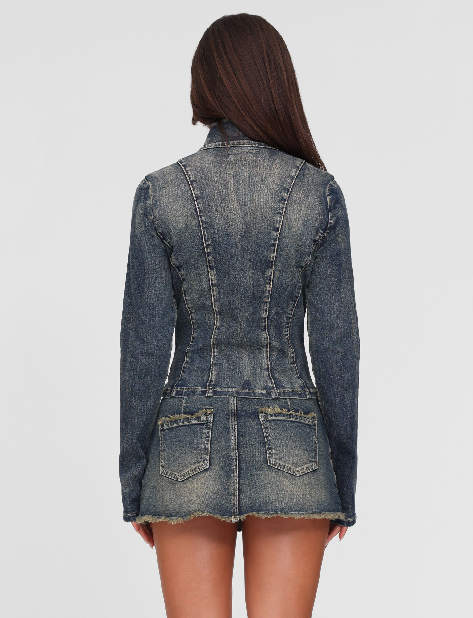 A woman with long brown hair is shown from the back, wearing the TIGERMIST OPHELIE JACKET in denim blue and a matching short denim skirt with frayed hem against a plain light gray background.