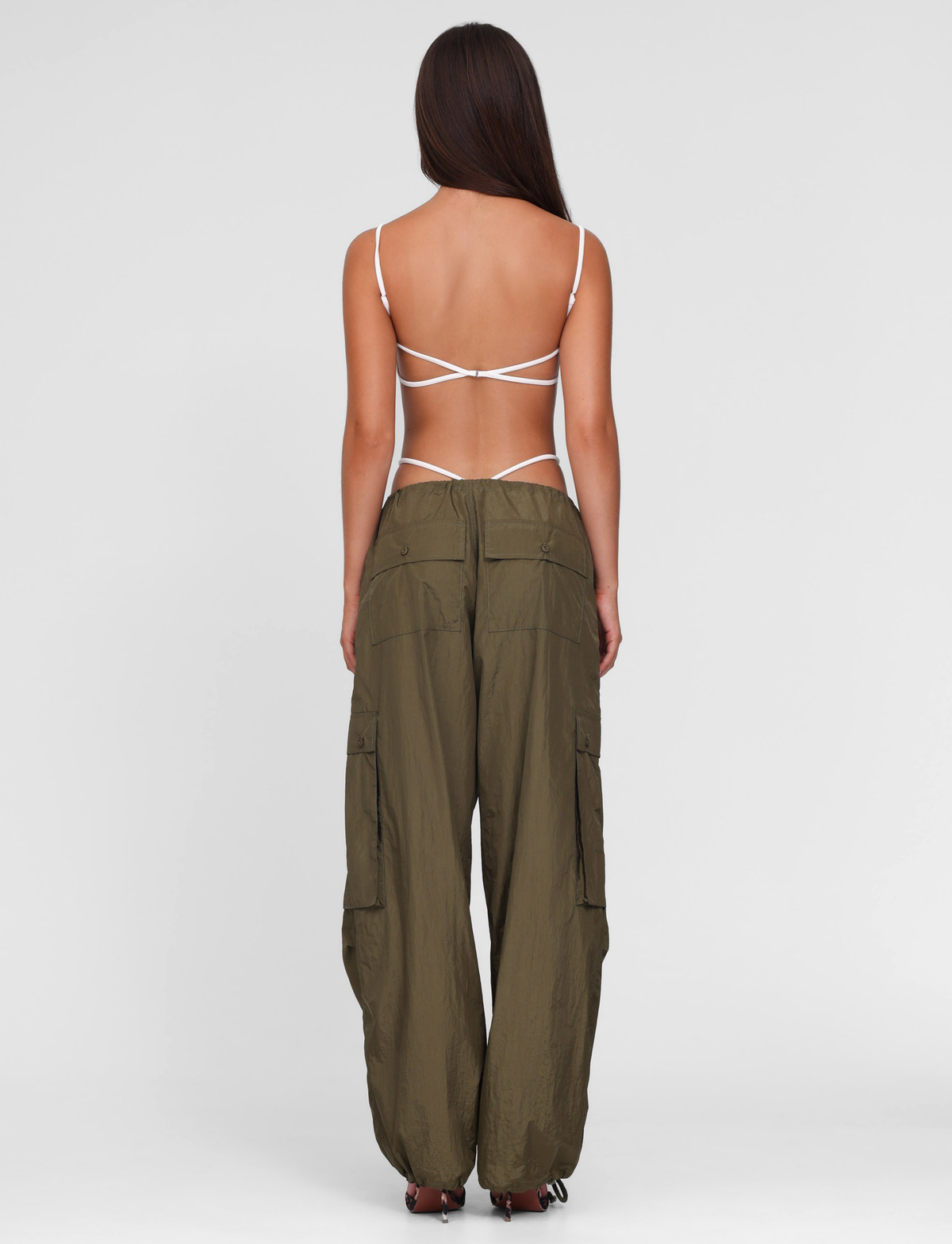 A woman faces away in a white strappy backless top and TIGERMIST VIOLETTE PANT - GREEN: KHAKI GREEN cargo pants with large pockets, set against a plain white background.