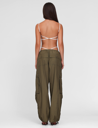 A woman faces away in a white strappy backless top and TIGERMIST VIOLETTE PANT - GREEN: KHAKI GREEN cargo pants with large pockets, set against a plain white background.