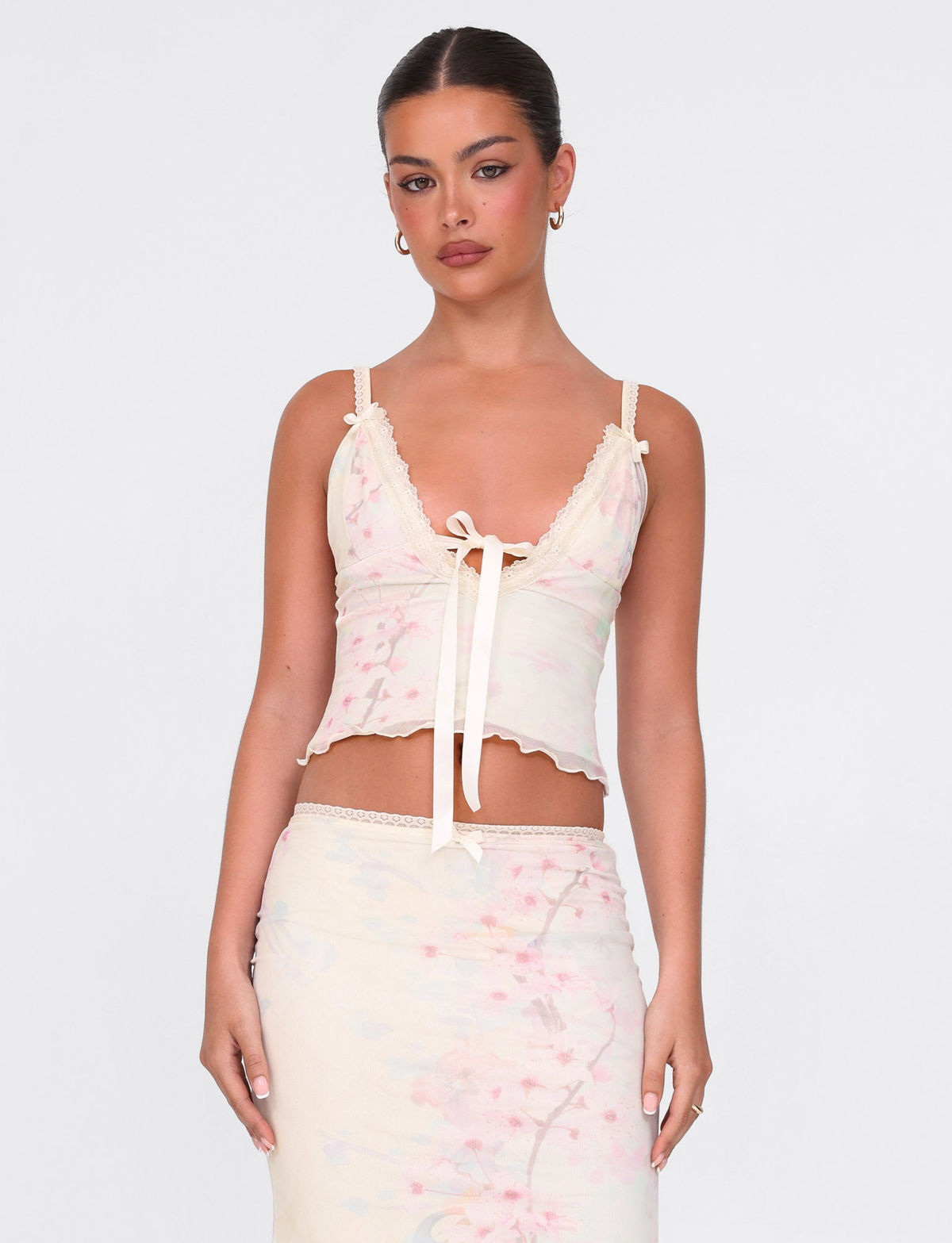 A woman wears the TIGERMIST LONIE TOP in washed cherry blossom floral print, featuring a center bow, paired with a matching skirt, standing against a plain white background.