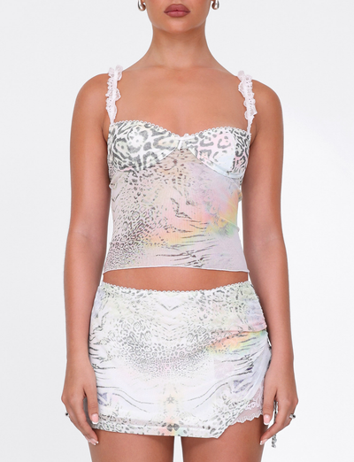 A woman wears the TIGERMIST JOSEPHINE MINI SKIRT in white animal print—featuring ruched side seams and iridescent pastel tones—with a lace-trimmed cami, standing against a plain white background.