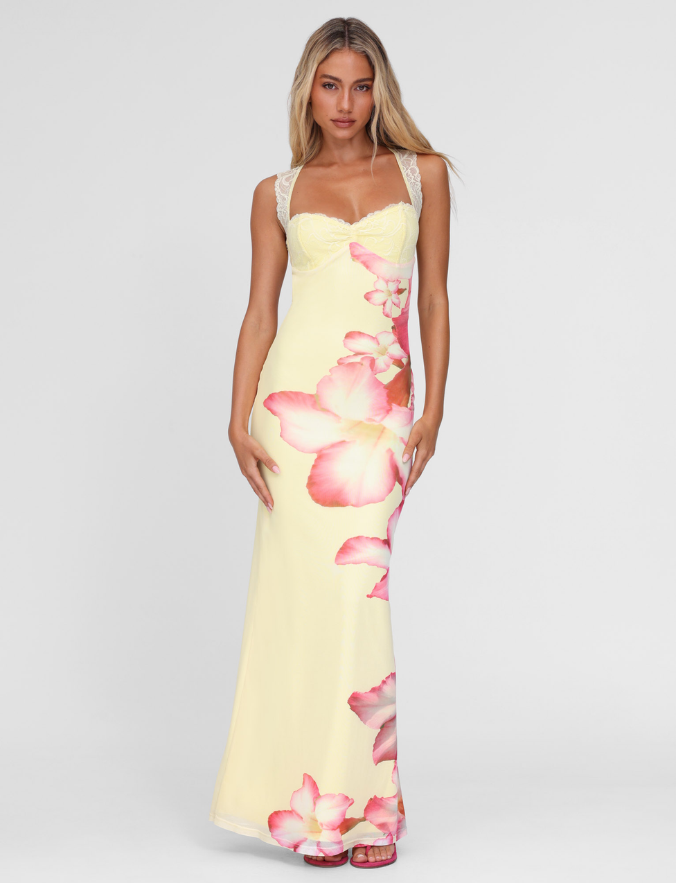 A woman with long blonde hair and a neutral expression models the TIGERMIST NYOMI MAXI DRESS in Yellow Hibiscus macro floral print, featuring lace bust panel and straps, against a plain background.