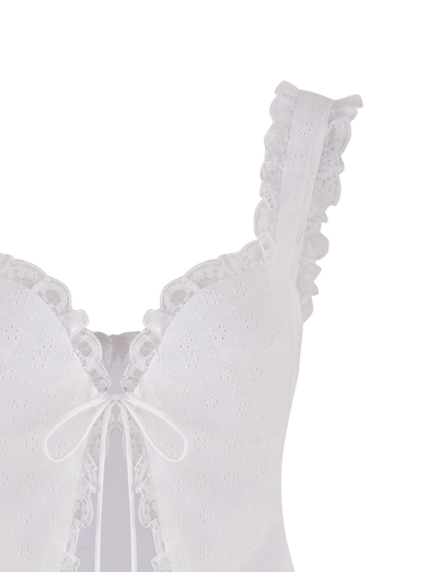 The KYANA TOP - WHITE by TIGERMIST is a cropped camisole featuring thin straps, scalloped lace trim, a front bow, and embroidered floral eyelets for a delicate, feminine look.