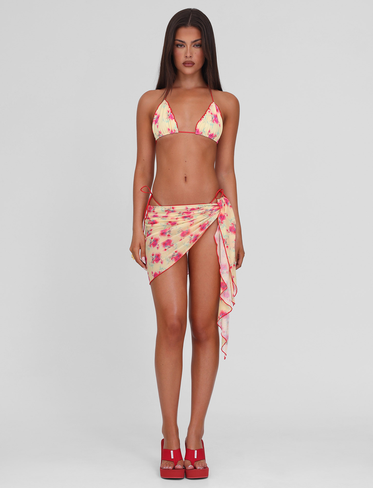 A woman with long, straight brown hair and a neutral expression models the TIGERMIST AMALIE 2PC BIKINI BOTTOM in Summer Blossom against a plain background, paired with a matching sarong and red platform sandals.