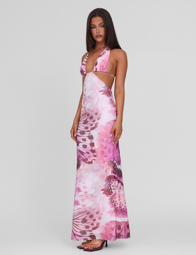 A woman poses against a plain background wearing the TIGERMIST SOLEIL MAXI DRESS - MACRO BUTTERFLY, featuring adjustable halter ties, side cutouts, and black heels.