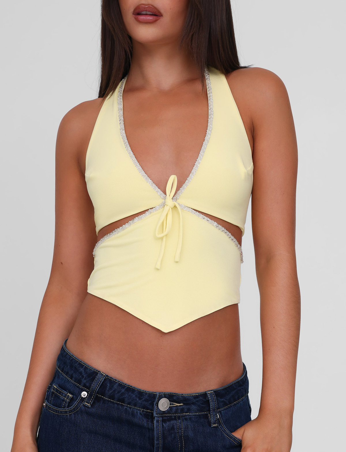 A woman wears the TIGERMIST LIZZIE TOP in lemon—a light yellow halter with a deep V-neck, beaded trim, and front tie—paired with dark blue jeans. The image is cropped from shoulders to hips.