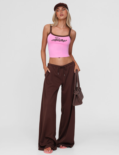 A woman wearing the TIGERMIST MERRYN TANK in pink with brown wide-leg pants, pink sandals, a brown cap, and a brown bag stands against a plain white background.