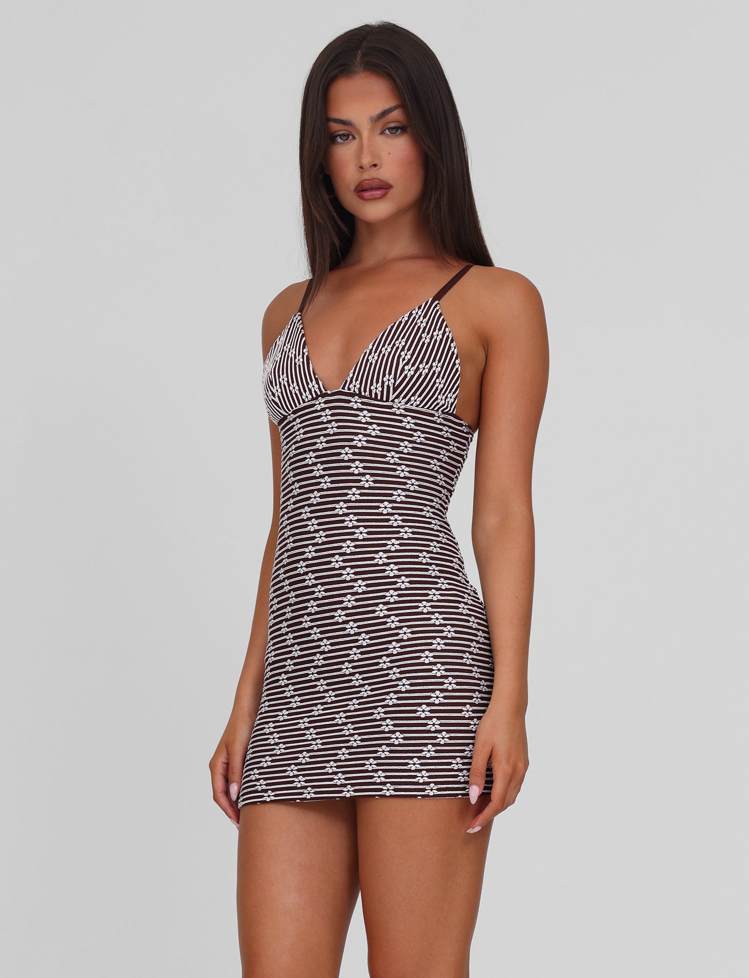 A woman with long dark hair models the TIGERMIST SAHRA MINI DRESS in chocolate brown stripe, standing against a plain light gray background and looking directly at the camera.