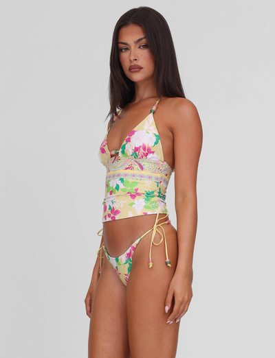 A woman with long dark hair wears the TIGERMIST FINLEA TANKINI TOP - PAISLEY BORDER and matching bikini bottoms with side ties, standing against a plain light gray background.