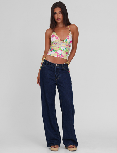A woman with straight brown hair wears the TIGERMIST FINLEA TANKINI TOP - PAISLEY BORDER, paired with wide-leg dark blue jeans and platform sandals, standing against a plain light gray background.