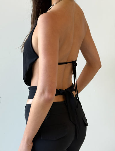 A woman wears the TIGERMIST EVANNA TOP in black, featuring a gathered bodice and halter design, paired with high-waisted black pants, shown in profile against a plain light background.