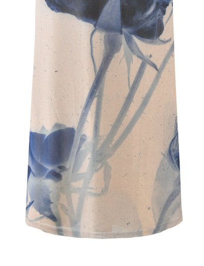 A close-up of the TIGERMIST JANIS MAXI SKIRT - INDIGO FLORAL shows semi-transparent fabric with large blue floral designs and stems on a light beige background.