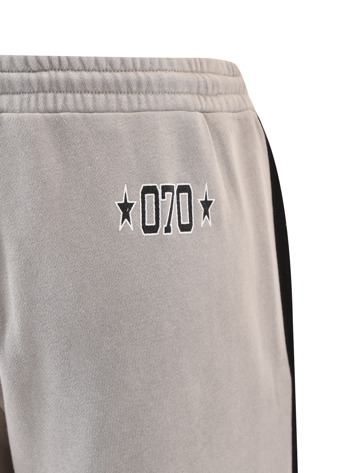 Close-up of TIGERMIST PAYTON TRACKPANT - STONE: grey cotton trackpants with "070" and stars embroidered in black on the left hip, plus a black vertical stripe down the side for a sporty look.
