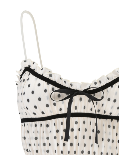 Close-up of the TIGERMIST LIORA TOP - POLKA DOT, featuring a white sheer fabric with polka dots, ruffled trim, thin adjustable straps, and a small black ribbon bow at the neckline.