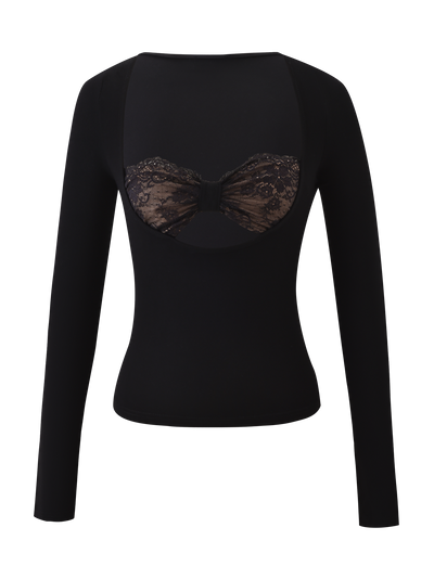 The DAMELA LONG SLEEVE TOP by TIGERMIST features black fabric, a sheer chest panel, and a decorative lace bandeau bow across the chest, shown on a white background.