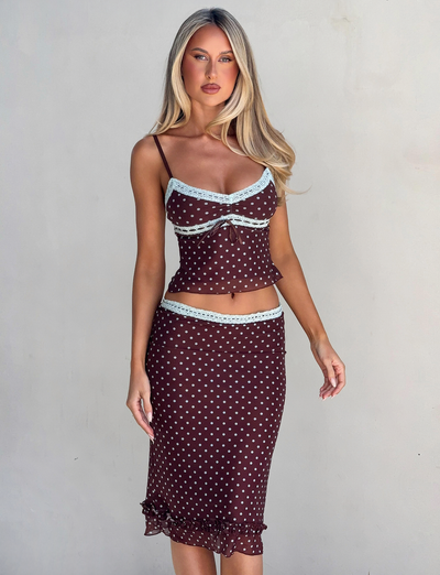 A woman with long blonde hair models the TIGERMIST AMARA MIDI SKIRT - POLKA DOT, a brown two-piece outfit with light blue trim and spaghetti straps, against a plain light background.