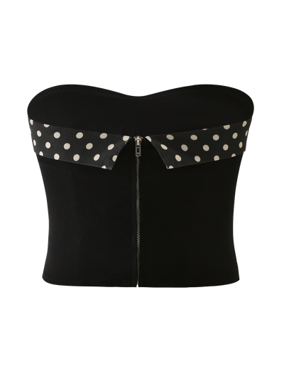 The KITTIE 2.0 BUSTIER by TIGERMIST is a black strapless corset top in suiting fabric, featuring a front zipper and a folded-over collar with a white polka dot pattern.
