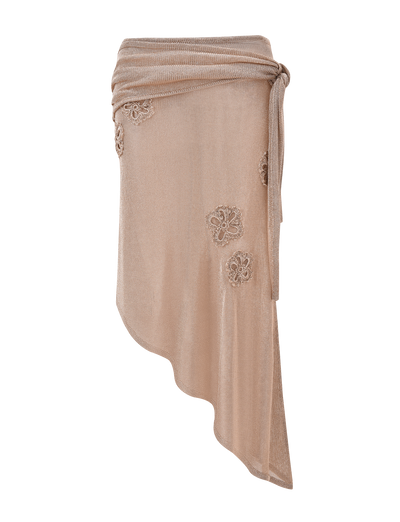 The ISATANA SKIRT - GOLD by TIGERMIST is a beige asymmetrical wrap skirt featuring a waist tie and floral lace appliqués on the front, showcased against a plain white background.
