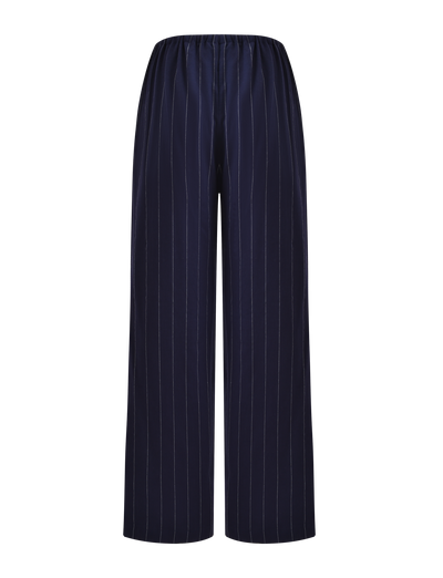 The LAINEY PANT - NAVY PINSTRIPE by TIGERMIST features a high-waisted, elasticated design with thin white vertical stripes. These wide leg linen pants blend comfort and style, shown against a white background.