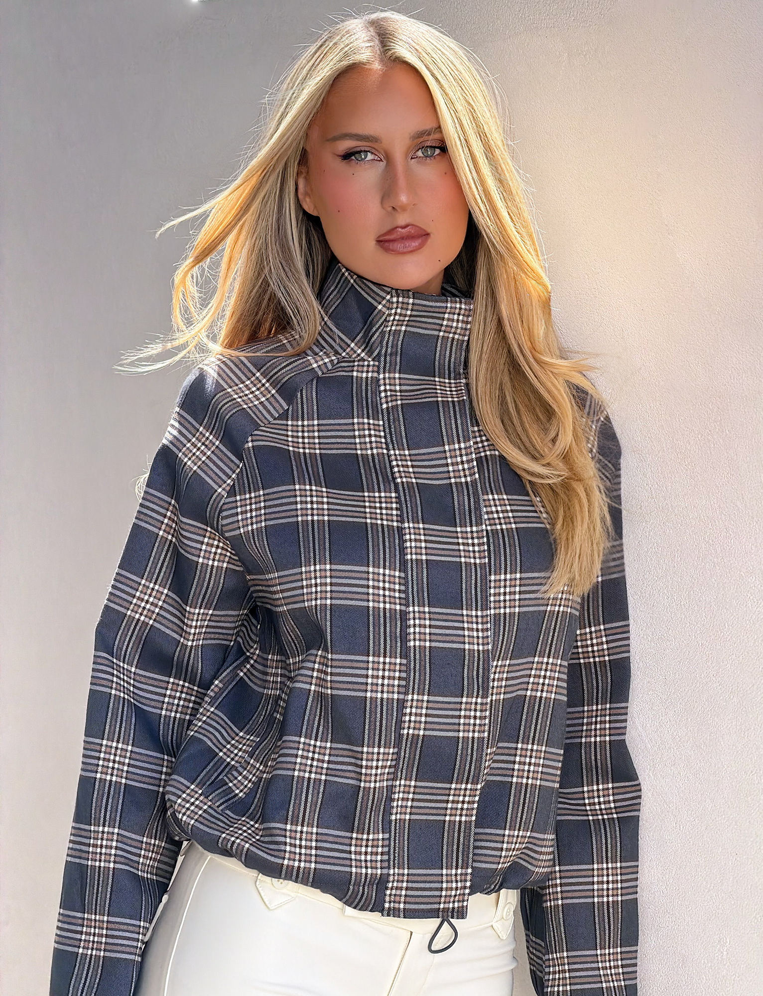 A woman poses in the TIGERMIST LENNEX JACKET - GREY CHECK, featuring an oversized fit and mock neck collar, effortlessly showcasing modern style.