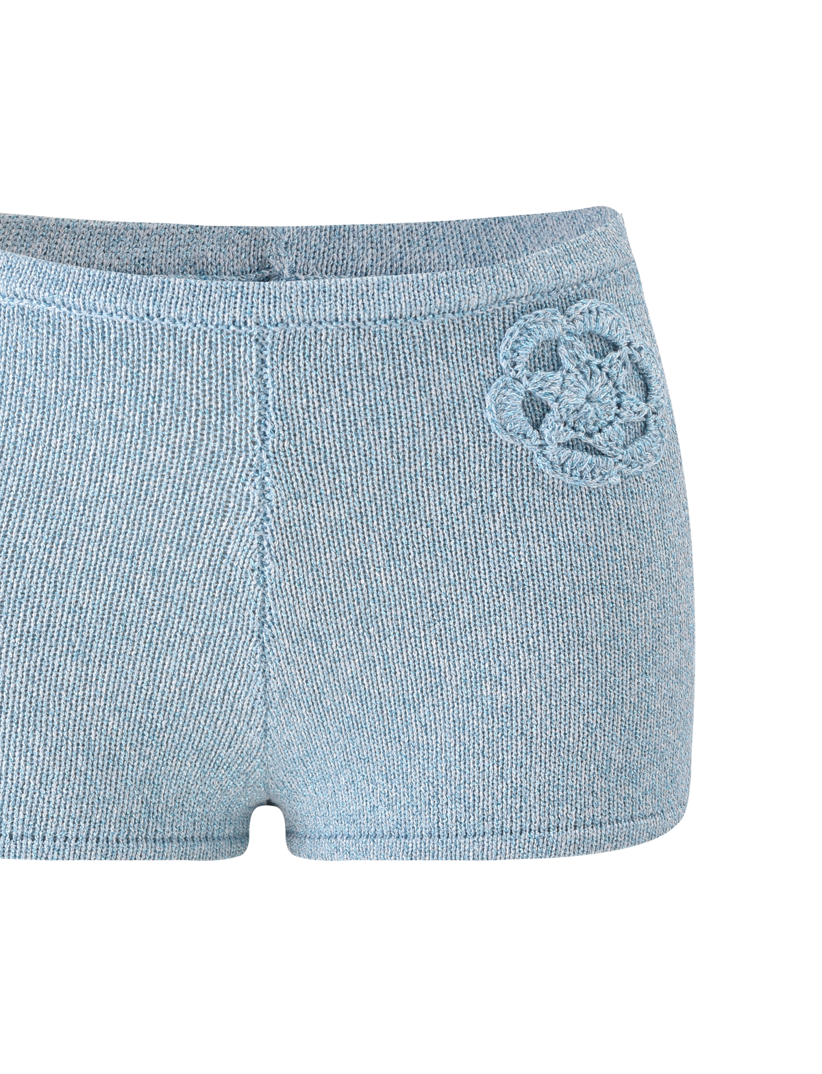 The SUNIA SHORT - BLUE by TIGERMIST is an ultra-mini light blue hot short with a decorative crocheted flower appliqué on the left hip, featuring a seamless, simple design and displayed on a white background.