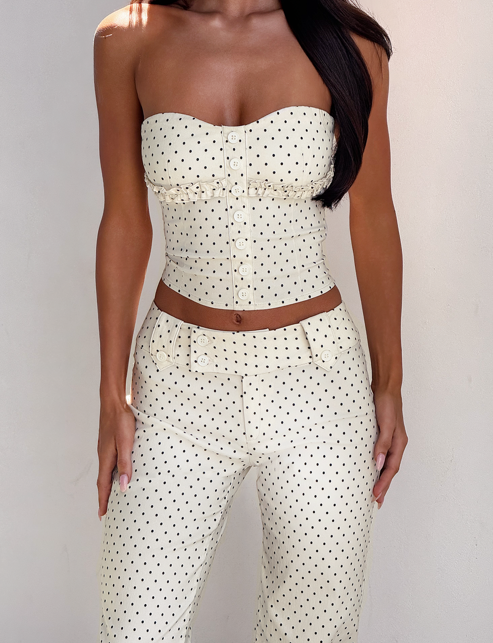 A woman models the TIGERMIST KITTIE PANT - CREAM DOT with a matching strapless, button-up top, standing against a plain light background. Her long dark hair is styled to one side.