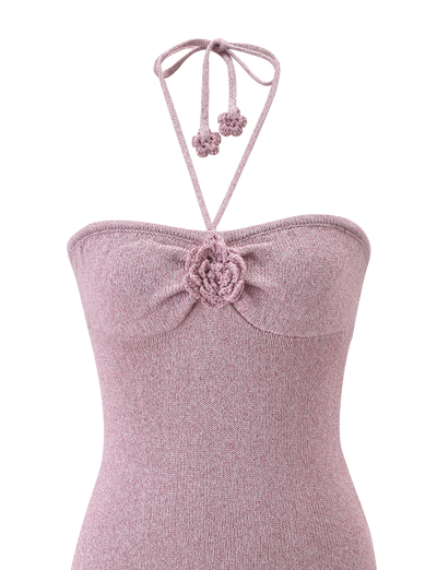 A close-up of the SUNIA DRESS - BABY PINK by TIGERMIST, a mauve knit halter dress with a gathered bust, crocheted flower detail with rose appliqué at the center, and neck tie strings.