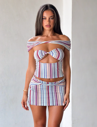 A woman with long brown hair models the TIGERMIST HAZE TWIST SKIRT - VARIEGATED STRIPE set, featuring a fitted off-the-shoulder striped top with a front cutout and matching mini skirt, standing against a plain light background.