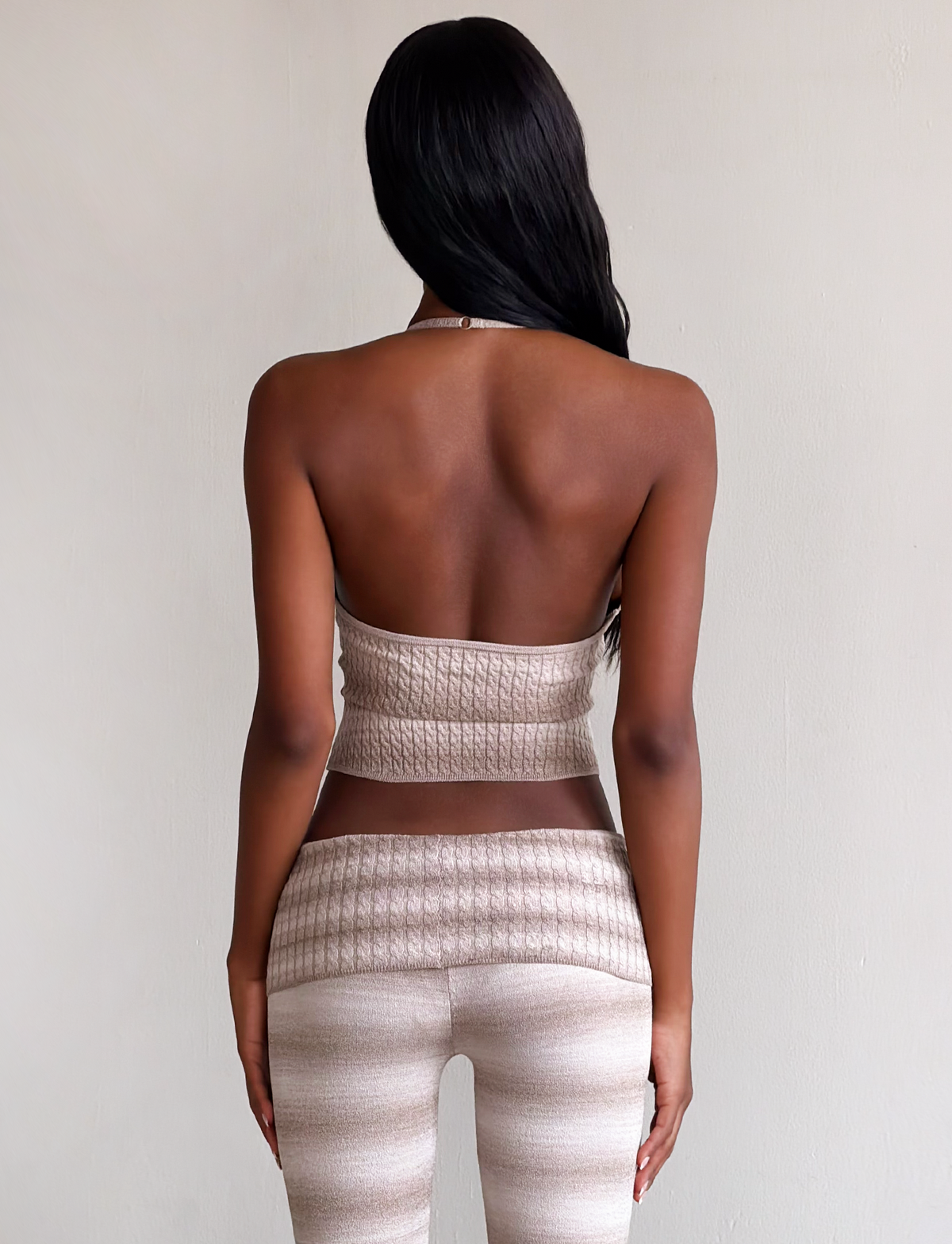 A woman with long dark hair stands facing away, wearing the TIGERMIST MARISSA KNIT CAMI in taupe ombre stripe and matching high-waisted pants against a plain light background.