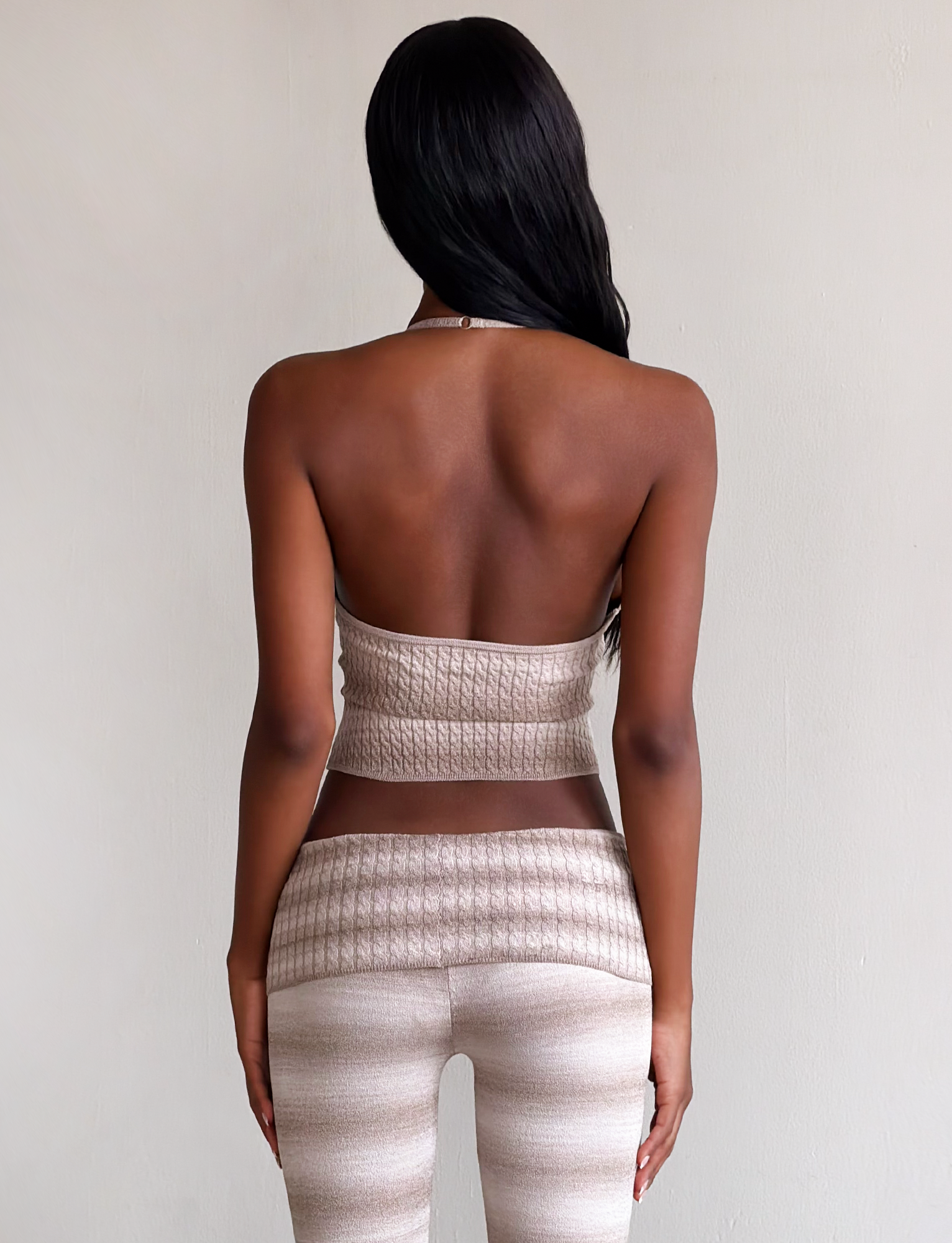 A woman with long dark hair stands facing away, wearing the TIGERMIST MARISSA KNIT CAMI in taupe ombre stripe and matching high-waisted pants against a plain light background.