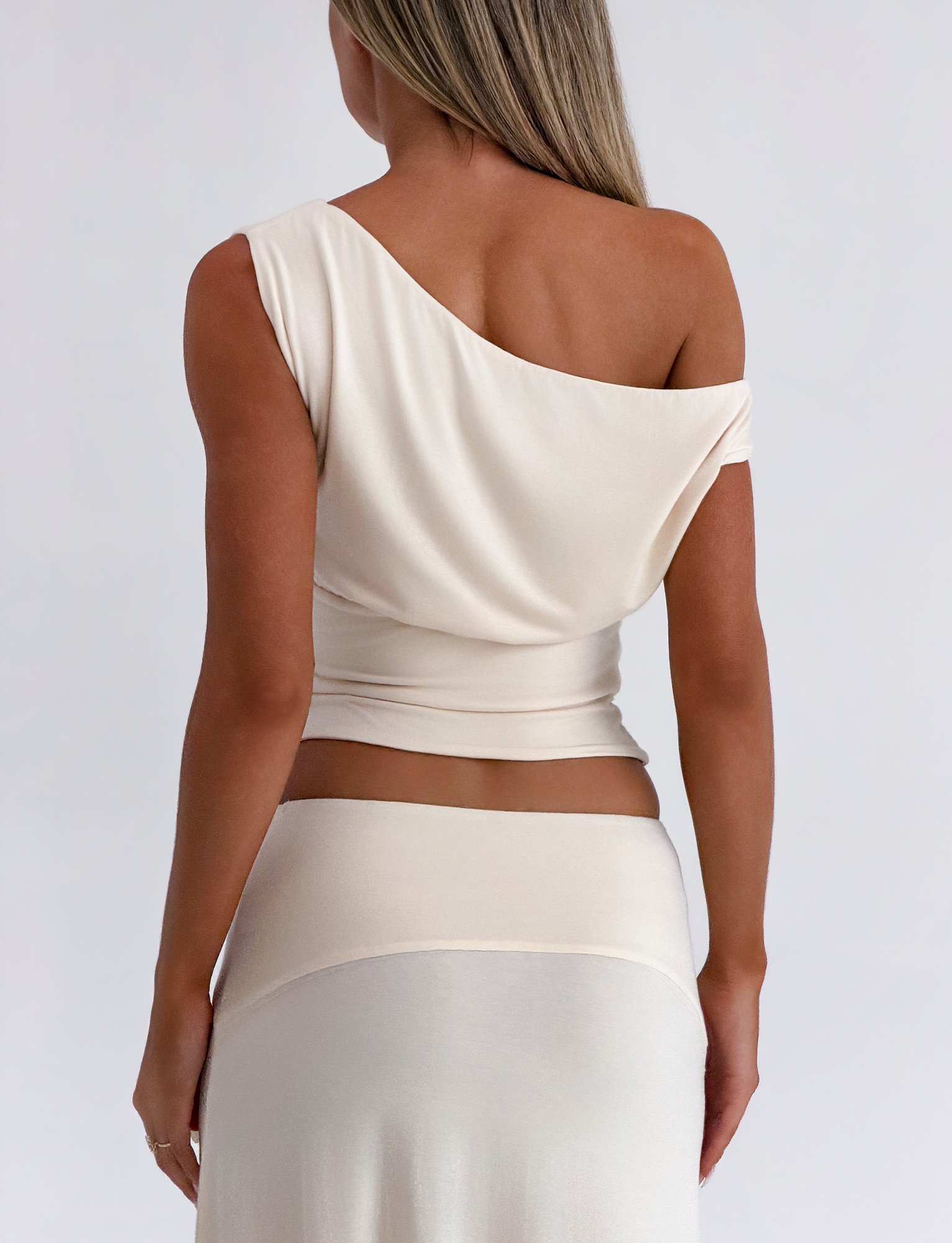 A woman with long, straight hair stands with her back to the camera in a cream TIGERMIST ALYSSA OFF SHOULDER TOP and matching skirt with a corseted waist, set against a plain, light background.