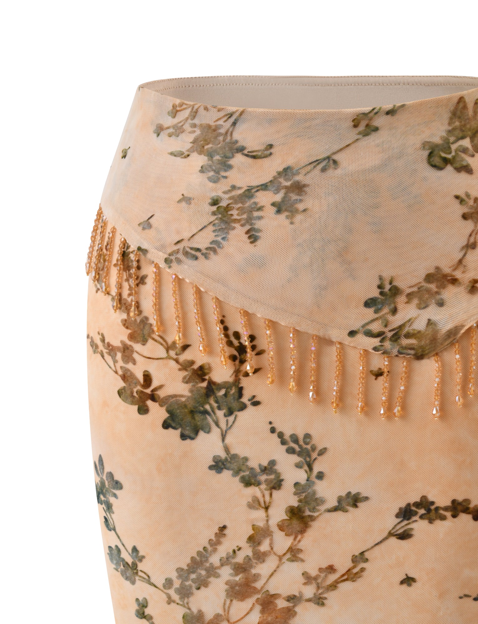 Close-up of the TIGERMIST OONA BURN OUT FRINGE SKIRT in tan, featuring a delicate green floral pattern and beaded fringe along an asymmetrical waist overlay, set against a white background.