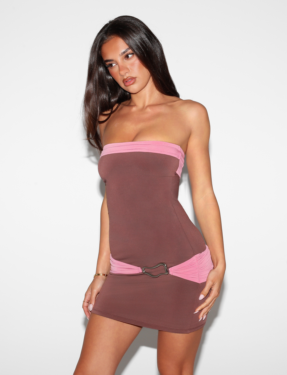 A woman with long dark hair models the Tiger Mist CL - EOS MINI DRESS, a strapless brown mini dress with pink accents, against a plain white background while looking to the side.