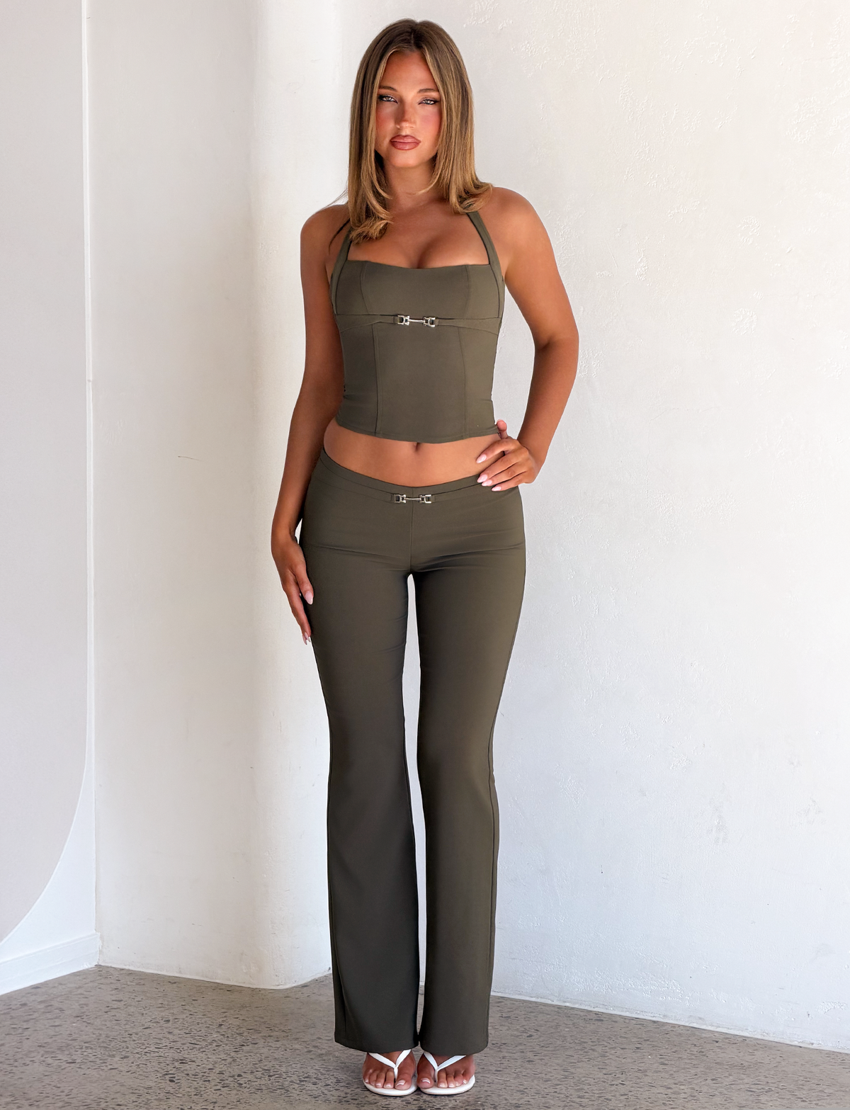 A woman wears an olive green KITTIE BUCKLE TOP with a silver buckle detail and matching low-rise flared trousers in a bodycon fit.
