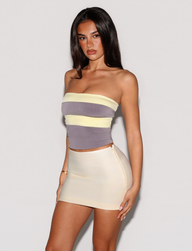 A woman with long dark hair wears the TIGERMIST EOS TOP in grey and yellow, featuring a strapless neckline and form-fitting silhouette, standing against a plain light background.