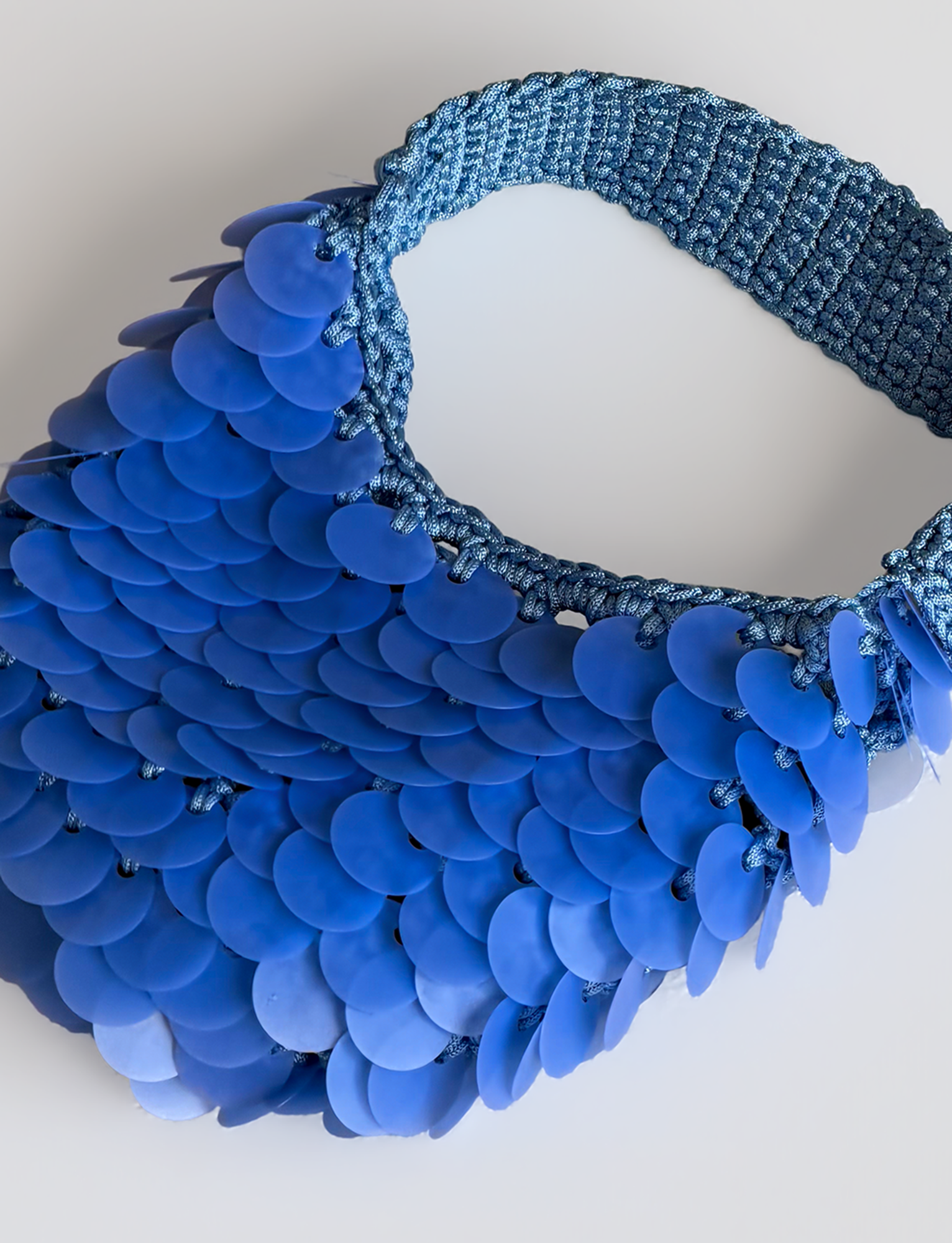 The CLEO BAG - BRIGHT BLUE by TIGERMIST features a vibrant blue crochet design with a woven strap and bold, overlapping shiny blue discs reminiscent of fish scales—making this standout beach bag the perfect blend of playful texture and eye-catching shimmer.