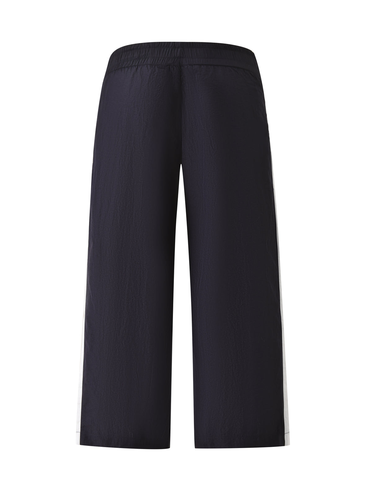 The SOPHIA WINDBREAKER CAPRI by TIGERMIST features a wide-leg silhouette in navy with an elastic waistband, crafted from lightweight windbreaker material for a subtly textured look. These ankle-length capris are designed with white vertical stripes down the sides, adding a sporty vibe. Shown from the back.