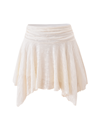The TIGERMIST MYLAH MINI SKIRT in ivory showcases eyelet lace, a ruched waistband, and an asymmetrical handkerchief hem, displayed against a plain white background.