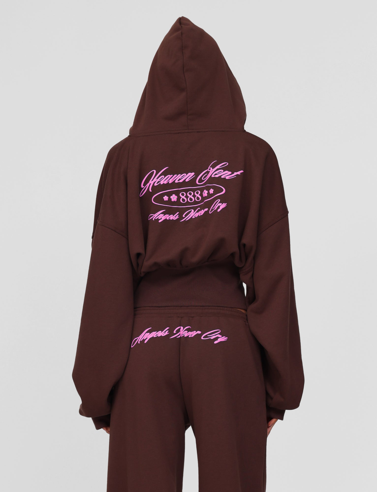 A person wears the TIGERMIST MERRYN HOODIE in chocolate, featuring pink custom puff print text on the back reading "Heaven Sent 888" and "Angels Never Cry"; matching pants have "Angels Never Cry" embroidered below the waistband.