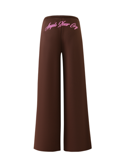 The MERRYN TRACK PANT - CHOCOLATE from TIGERMIST features a wide-leg fit, elastic waistband, and “Angels Never Cry” in pink script on the back—your must-have chocolate tracksuit piece for style and comfort.