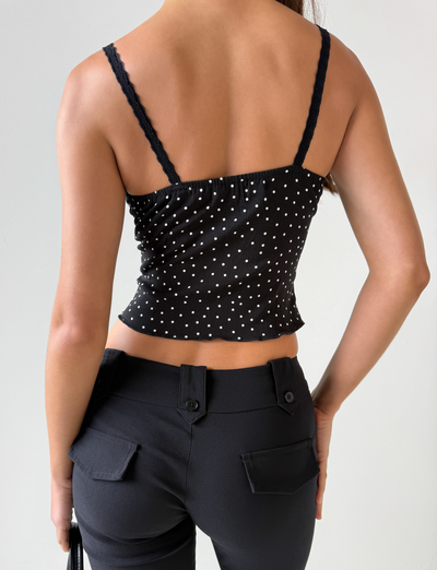 A person is shown from the back wearing the BAILEE CAMI TOP - BLACK POLKA by TOP ONE LADYS FASHION PTY LTD, featuring white polka dots and lace trim, paired with black pants against a plain light background.